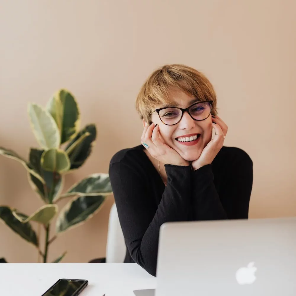 business woman at laptop with her head in her hands smiling